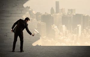 An elegant businessman with a paint roller transforming a brick wall into urban city landscape including tall buildings concept